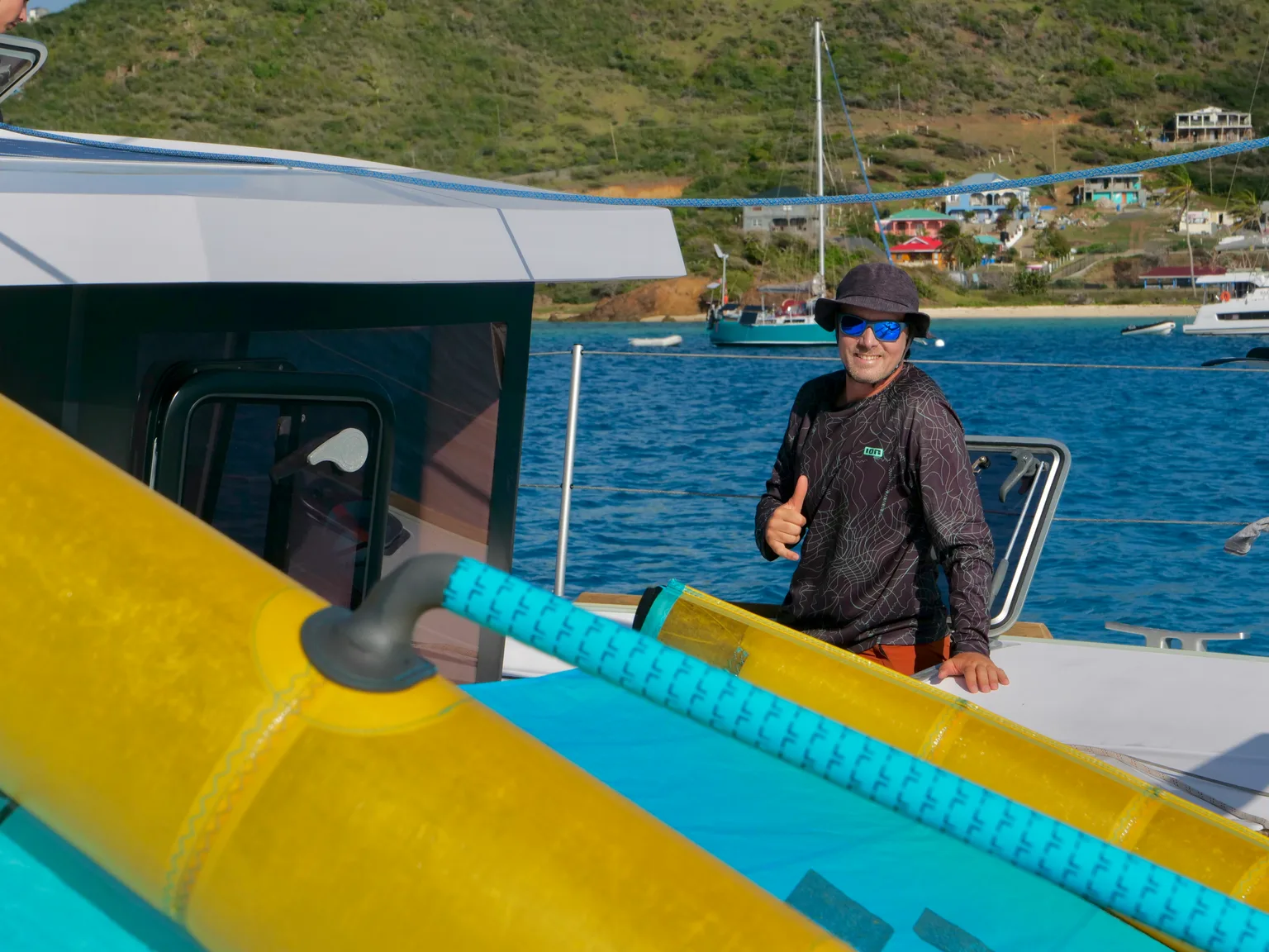 Alexis, pouce levé à bord d'un catamaran au mouillage, une aile de wingfoil gréée au premier plan